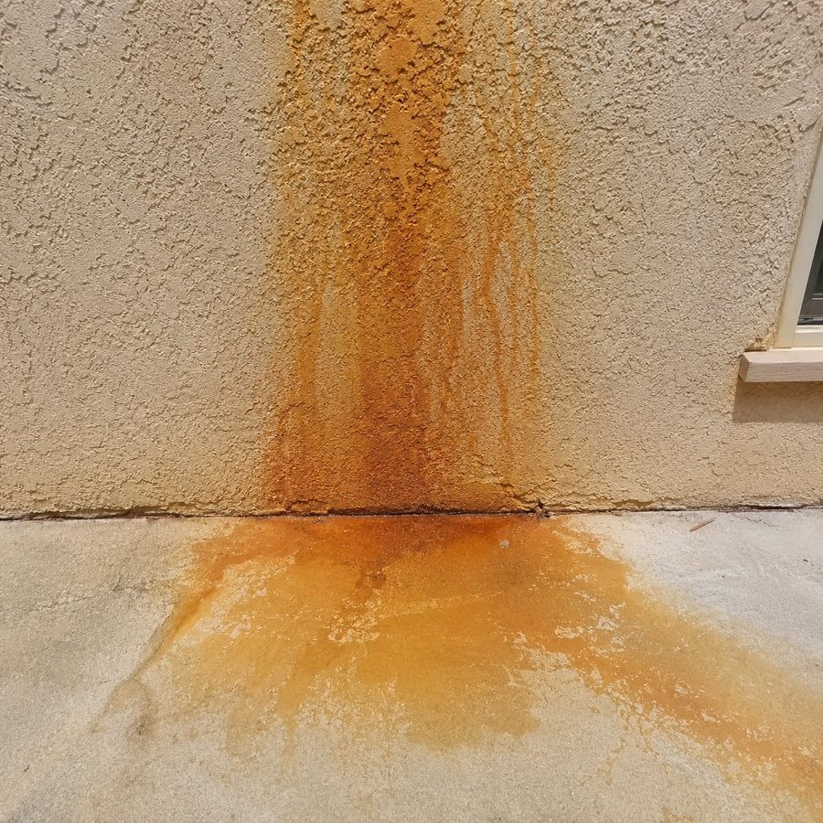 Orange sprinkler rust stains streaking down a stucco wall onto concrete